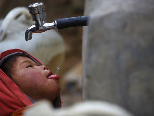 Một bé trai uống từng giọt nước ở vòi nước công cộng tại Nepal (Ảnh: Reuters)